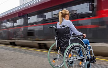 На фото девушка сидит в инвалидном кресле, а рядом проезжает железнодорожный поезд